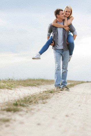 Happy young man giving piggyback ride to woman on trail at field